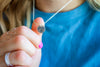 Person wearing a silver necklace with a round pendant, holding hands together.