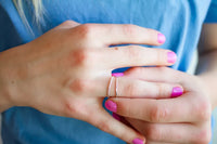 Close-up of a hand wearing 2 silver rings with pink nail polish on a blue background