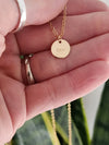 Gold necklace with a round pendant engraved with 'SAM' held in a hand.
