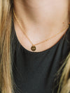 Gold necklace with a round pendant worn by a person against a black background