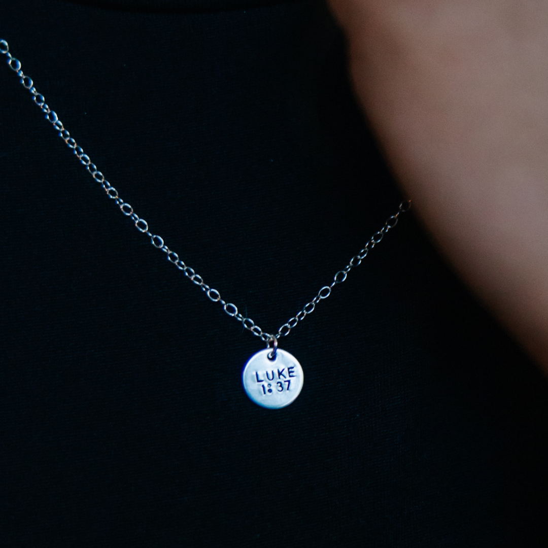 Necklace with a round pendant engraved 'LUKE 14:37' on a dark background