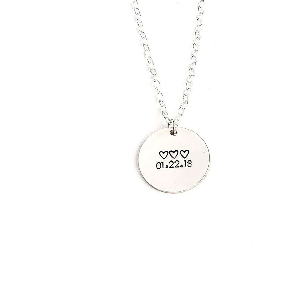 Silver necklace with a round pendant featuring hearts and numbers on a white background