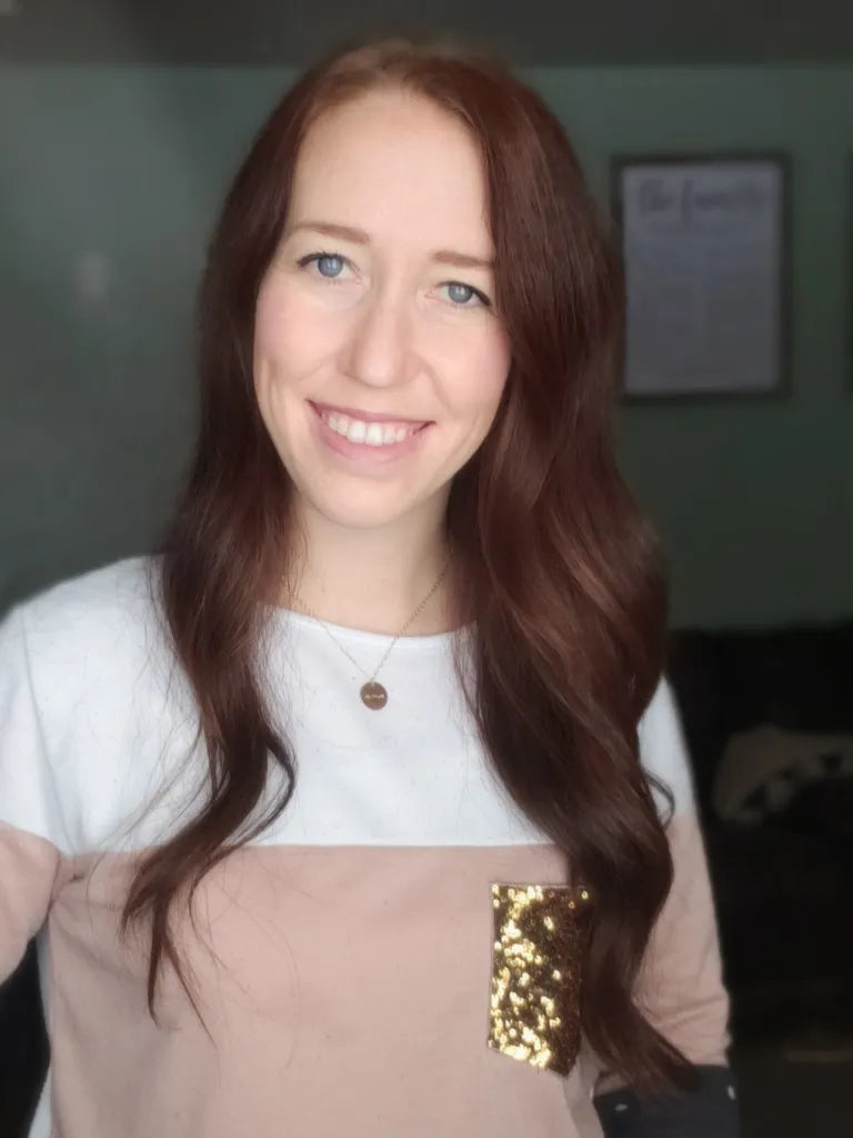 Woman with long brown hair wearing a white and beige top wearing a personalized necklace.