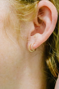 Close-up of an ear wearing a gold hoop earring with blonde hair.