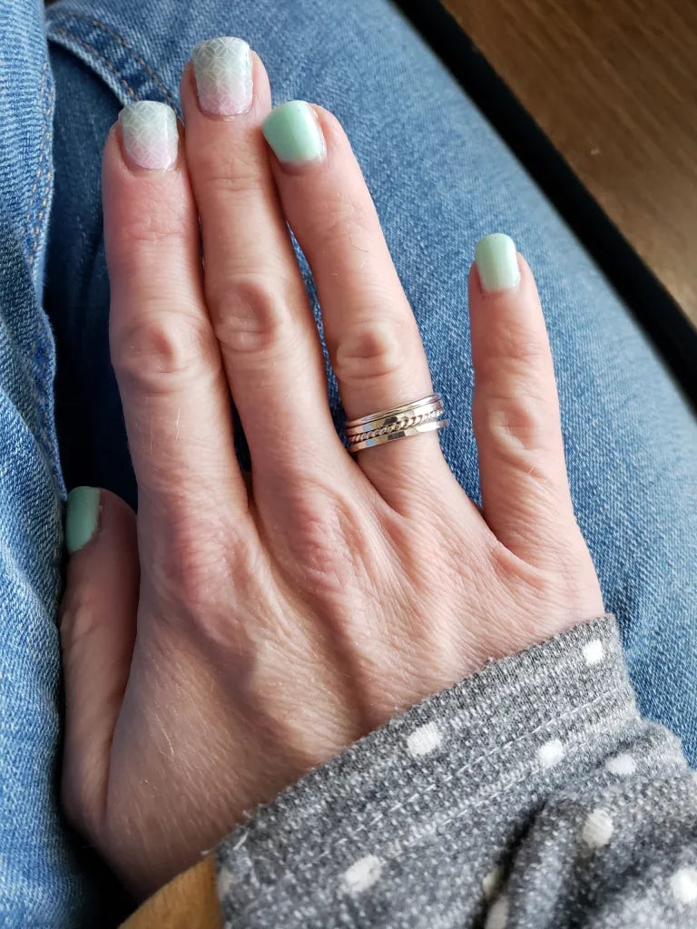 Hand with light green nail polish wearing a silver ring stack on a blue denim background