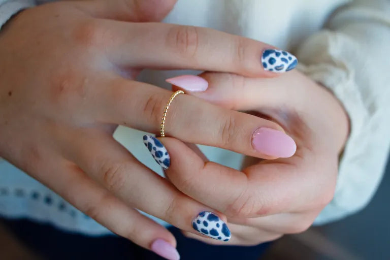 Close-up of hands with pink and blue nail designs wearing a gold ring.