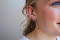 Close-up of a person wearing a gold hoop earring with a plain background