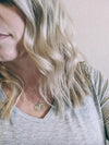 Close-up of a person with blonde hair wearing a gray shirt and a necklace with circular pendants.
