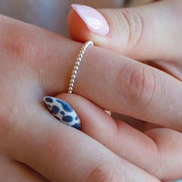 Close-up of a hand wearing a gold ring with a blue and white patterned nail.