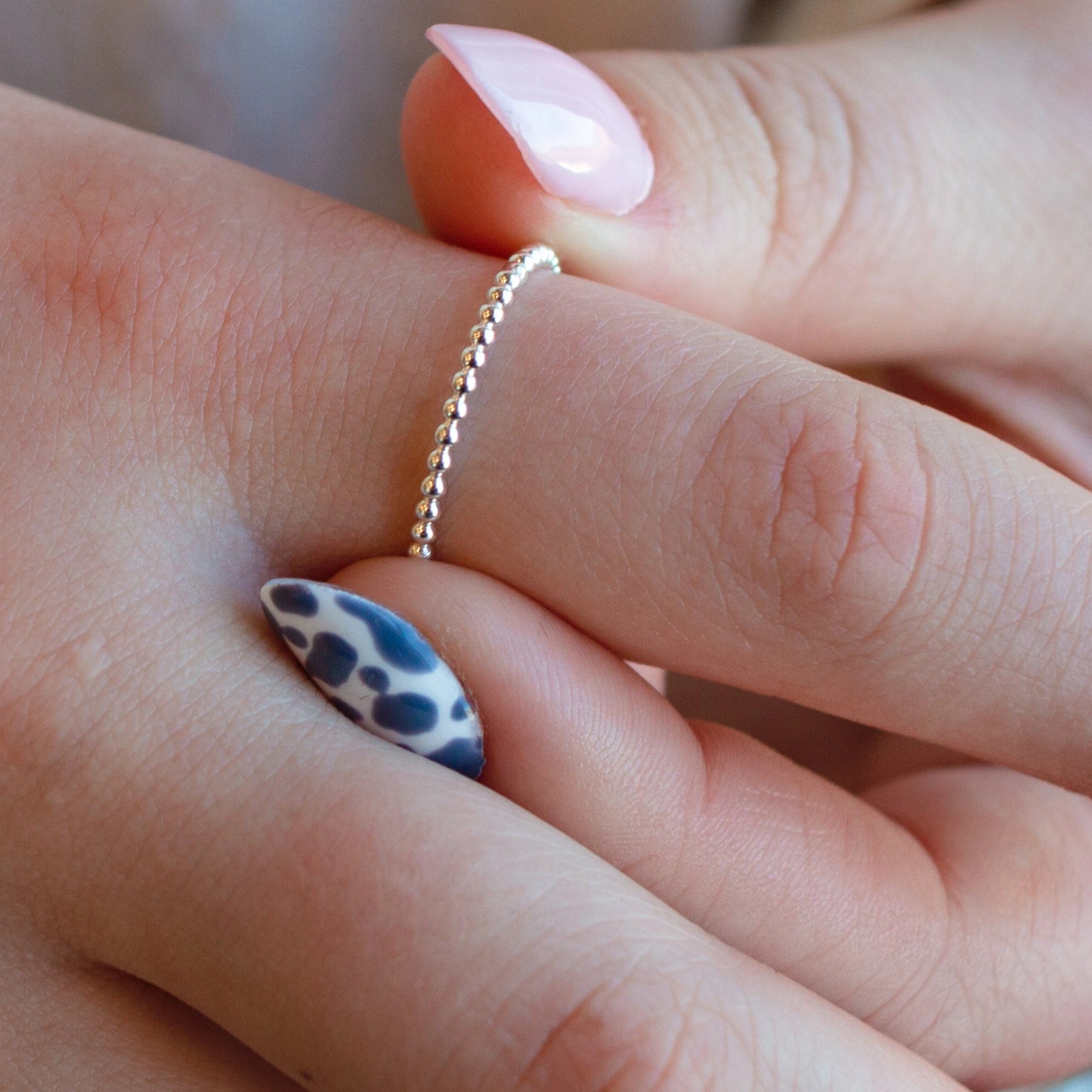 Close-up of a hand wearing a gold ring with a blue and white patterned nail.