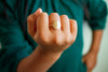 Hand wearing a gold ring with a blurred green shirt background