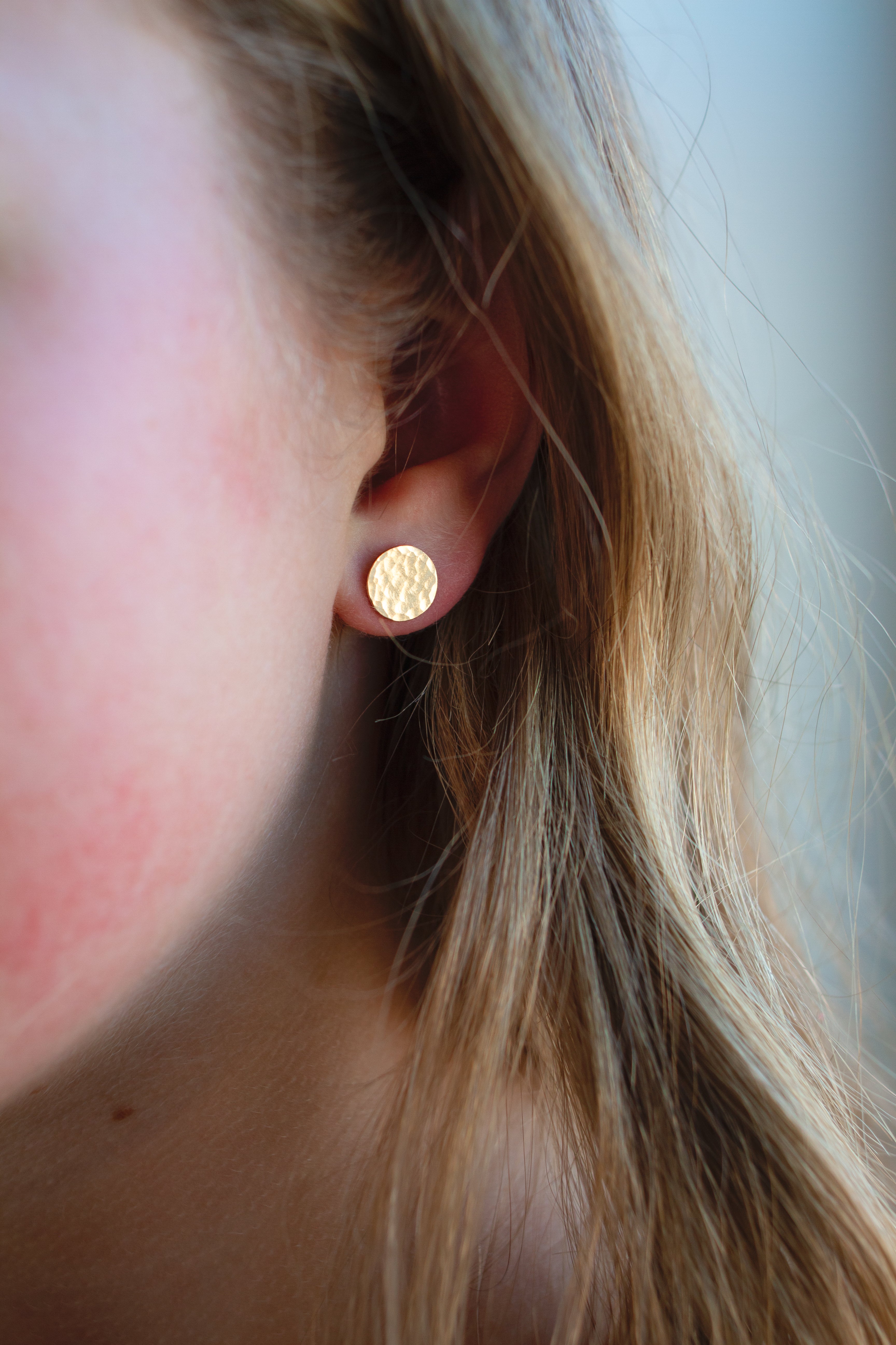Close-up of a person wearing gold round earrings with a neutral background