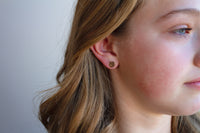 Close-up of a young girl wearing a gold earring with a plain background