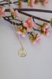 Necklace with a round pendant on a white surface with pink flowers in the background