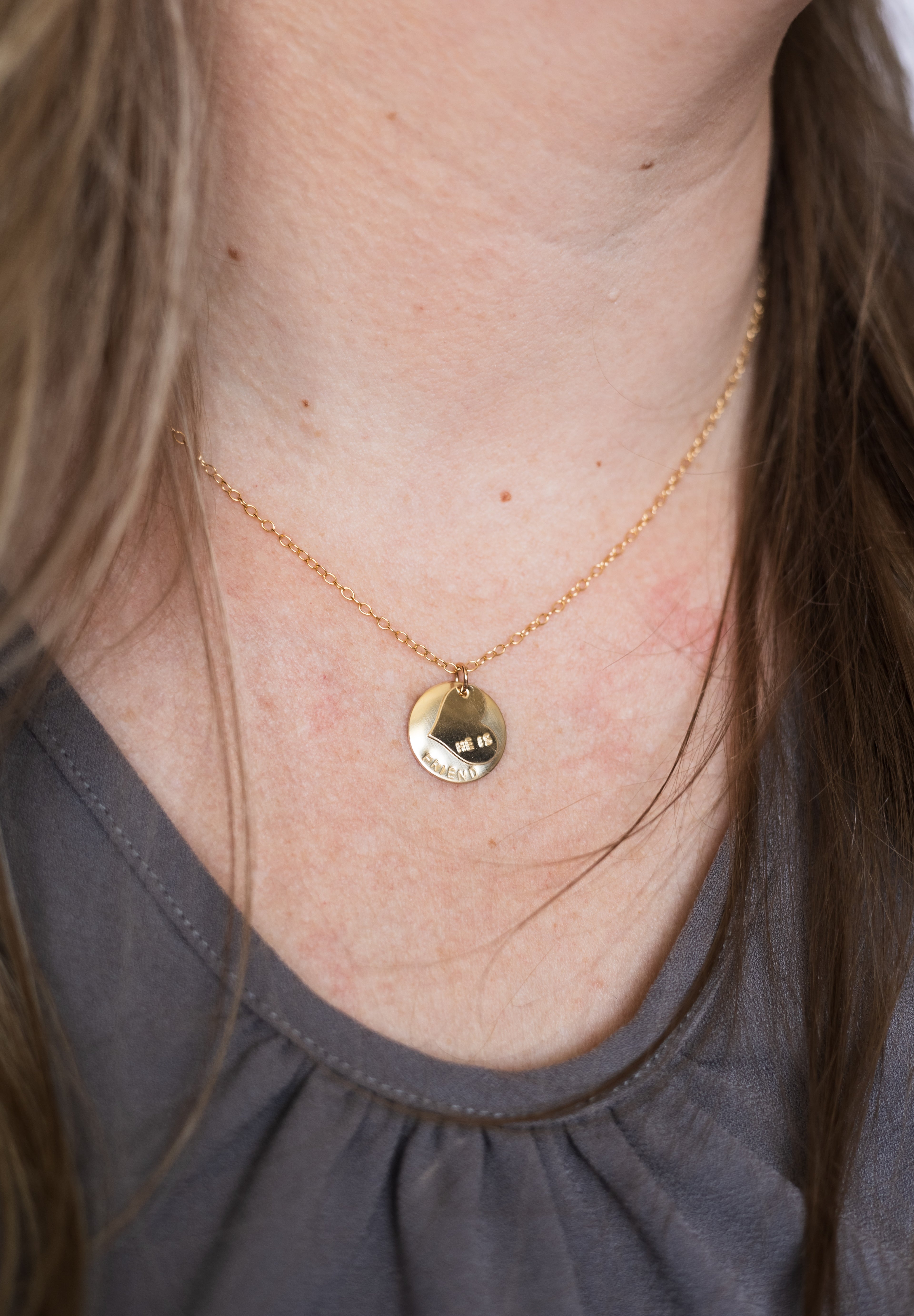 Gold necklace with a small round pendant on a person wearing a gray top.