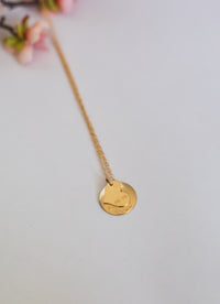 Gold necklace with a round pendant on a light gray background
