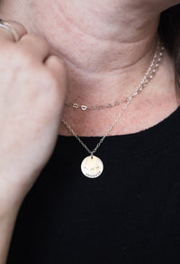 Close-up of a person wearing a delicate necklace with a round pendant on a plain background
