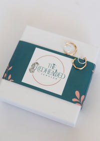 Jewelry box with 'The Redheaded Jeweler' logo and gold earrings on a white background