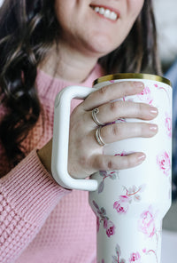 Person holding a floral-patterned mug with a pink sweater wearing rings
