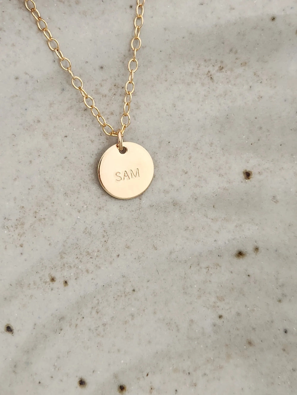 Gold necklace with a round pendant engraved with 'SAM' 