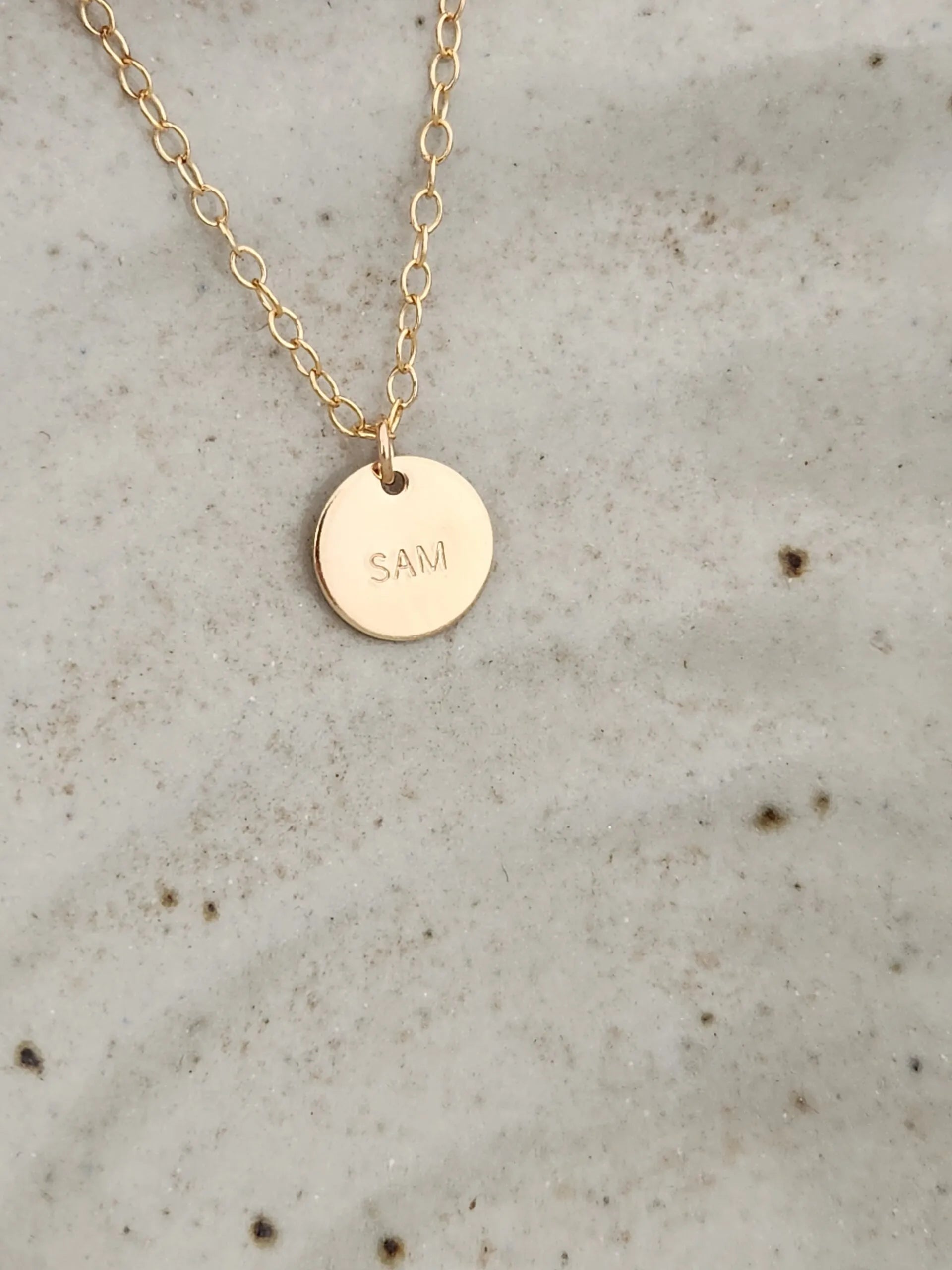 Gold necklace with a round pendant engraved with 'SAM' 