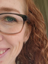 Close-up of a person with glasses and red hair, wearing earrings.