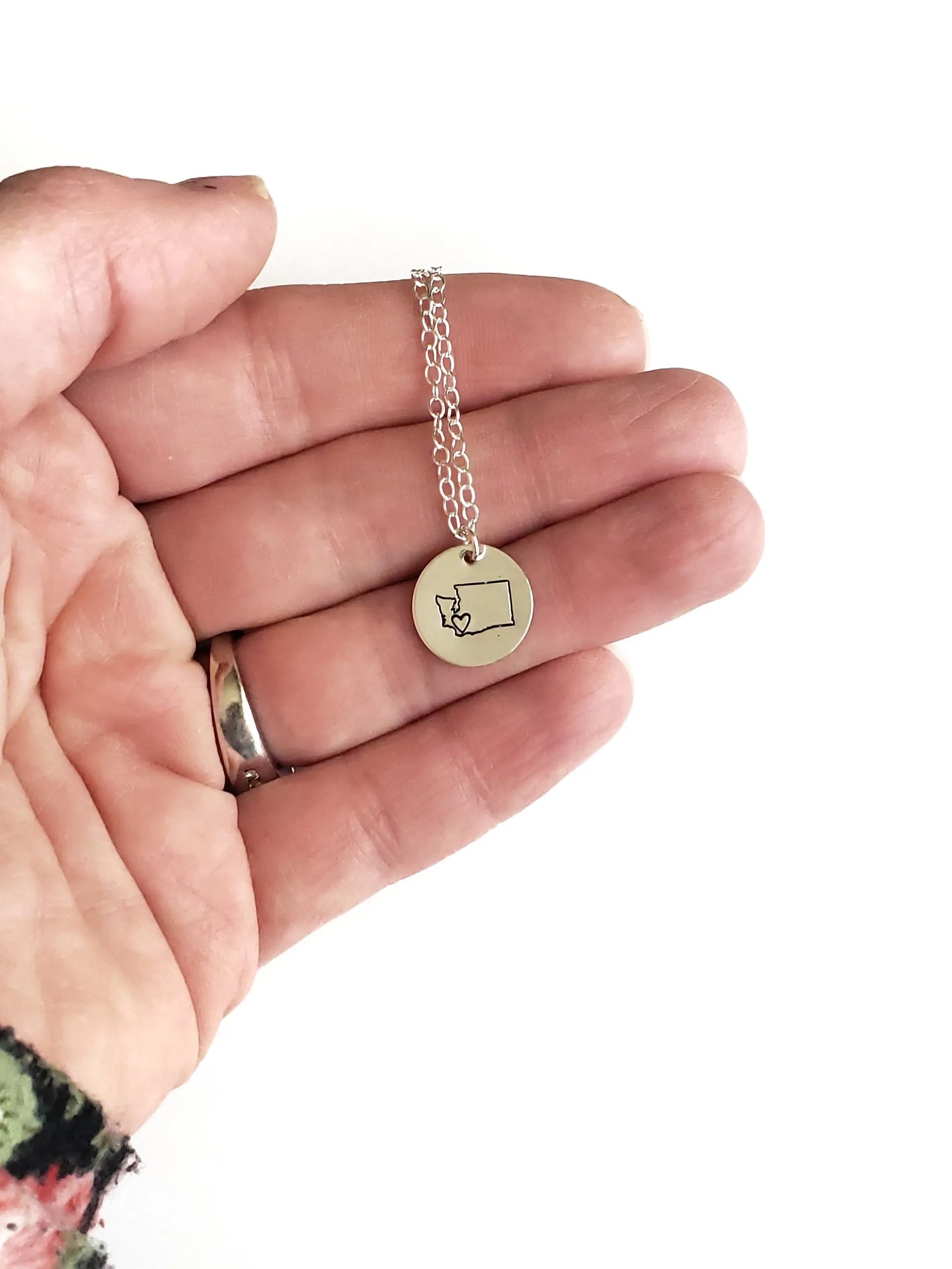 Hand holding a necklace with a small round pendant on a white background