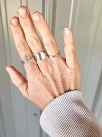Hand wearing multiple silver rings with a neutral background