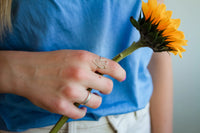 Person holding a sunflower with a blue shirt and heart-shaped ring.