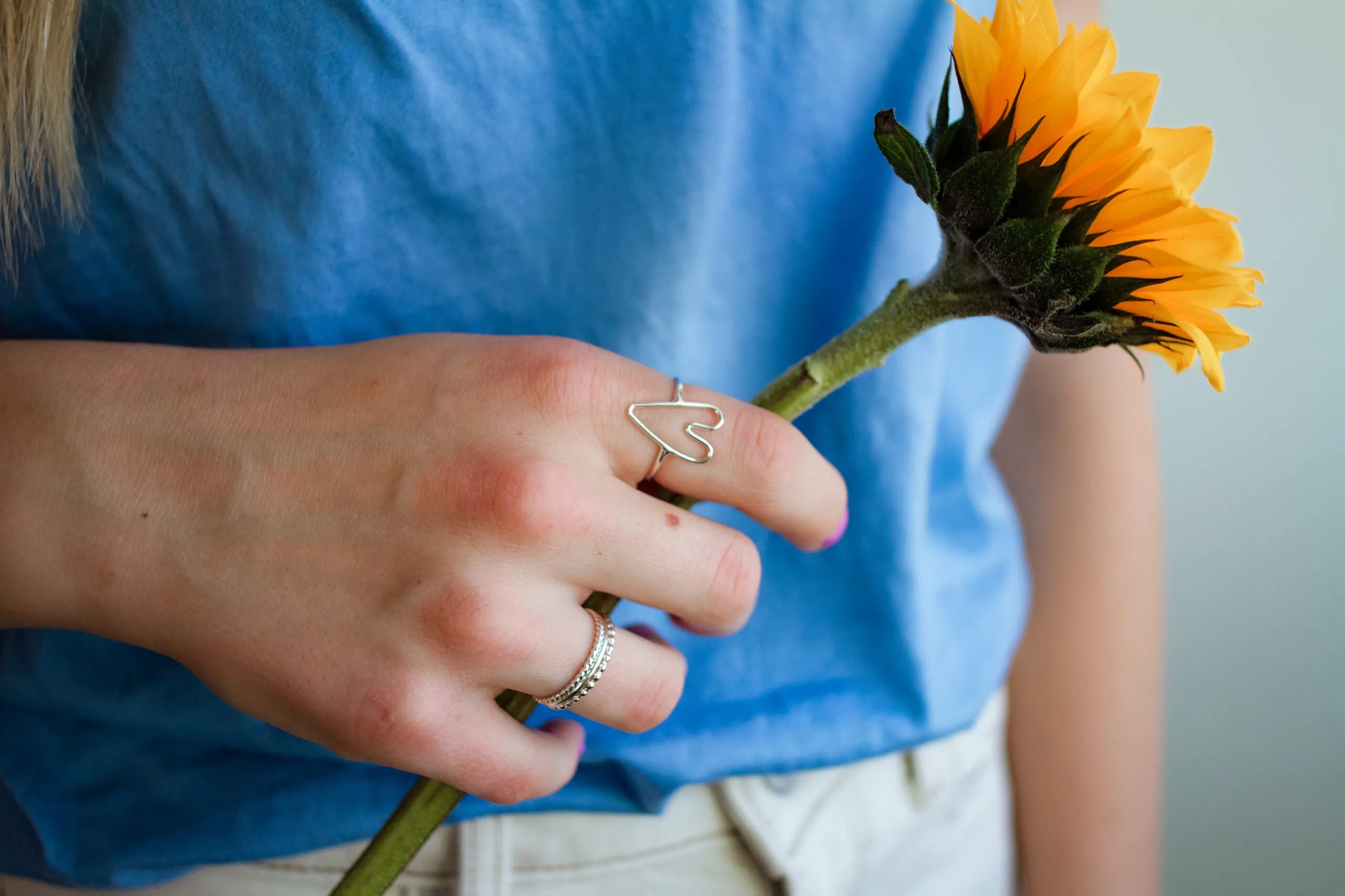 Person holding a sunflower with a blue shirt and heart-shaped ring.